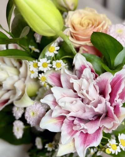 A close view of a double pink and white lily, a peach rose and white feverfew daisies