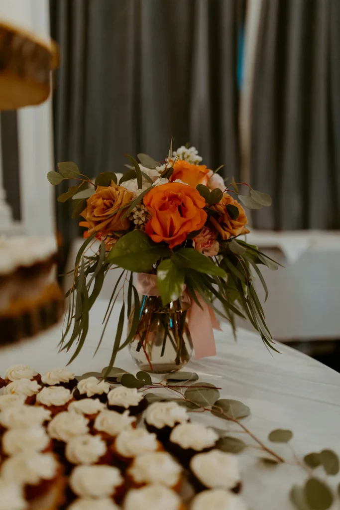 A small centrepiece of orange roses and greenery beside a tray of desserts.