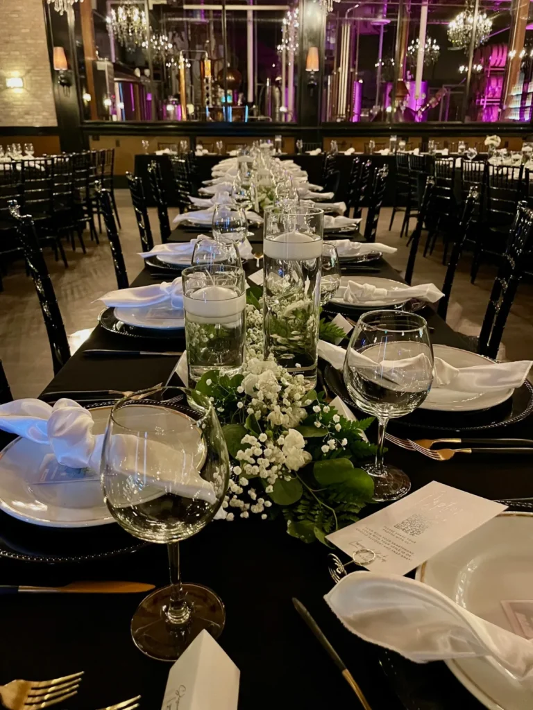 A long dinner table with clear vases of white flowers and baby's breath between the place settings.