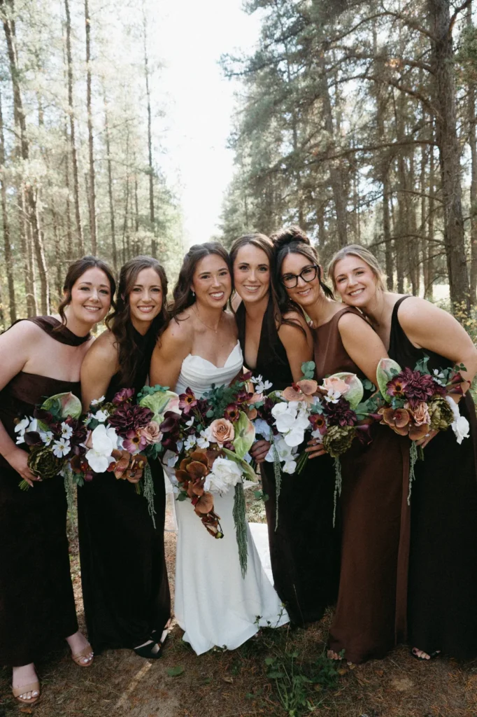 The bride with her bridesmaids in black dresses, all holding bouquets of burgundy, white and rust flowers.