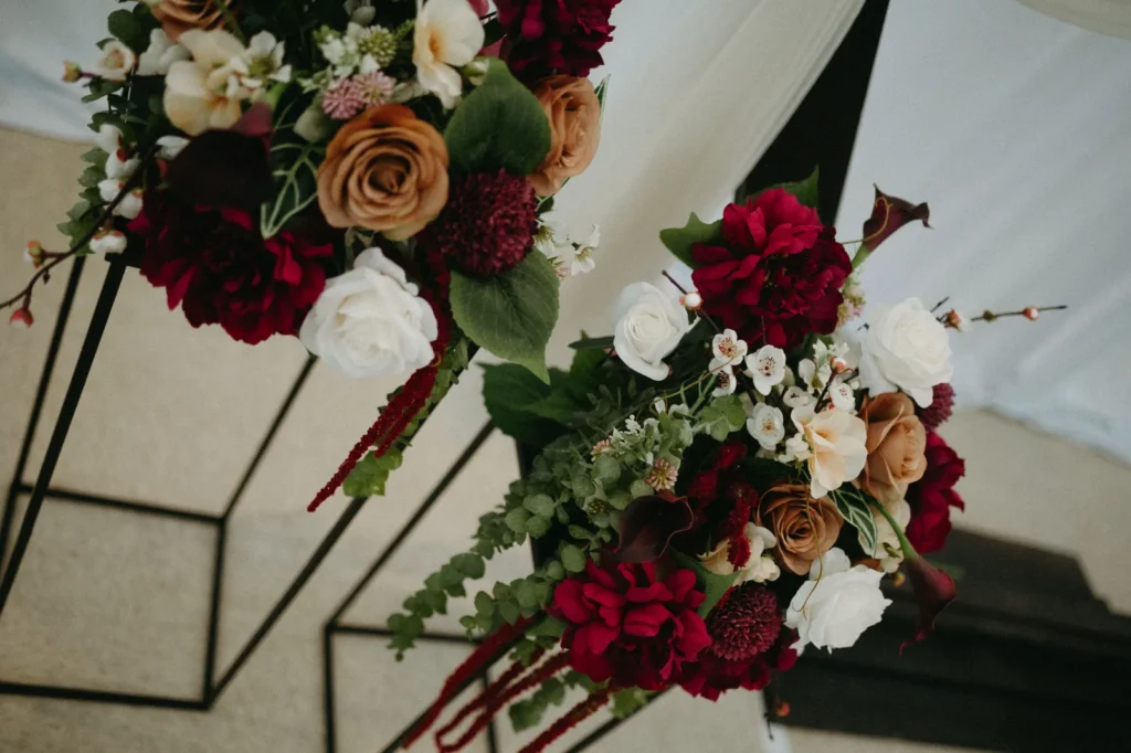 Burgundy roses, rust and white flowers on tall black metal stands, seen from below.