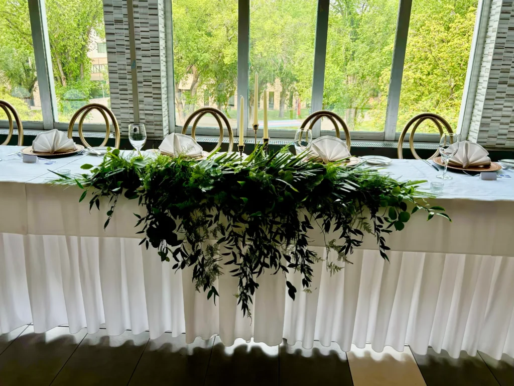 A long garland of greenery along the head table in front of tall windows.